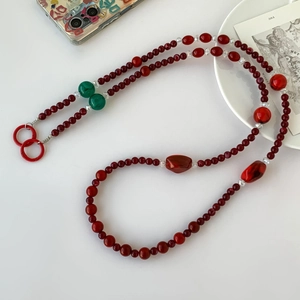 Lanière de téléphone en perles acryliques rouge foncé avec accents verts sur fond blanc