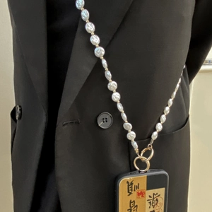 Dettaglio tracolla per cellulare in perle barocche con chiusura dorata su blazer nero