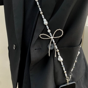 Detail of crossbody phone strap with white pearls and a bow on black suit background