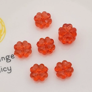 Detail of red clover-shaped faceted acrylic beads scattered on a white ceramic plate