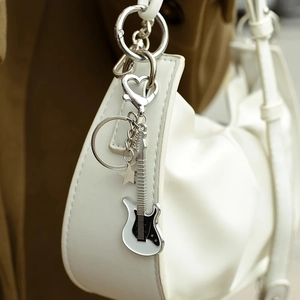 Detailed shot of a white electric guitar keychain with heart-shaped clip on a leather bag