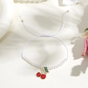 Dettaglio ravvicinato di un ciondolo a ciliegia su un bracciale di perle bianche regolabile