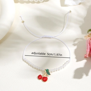 Dettaglio del ciondolo a ciliegia su bracciale regolabile di perle bianche e oro