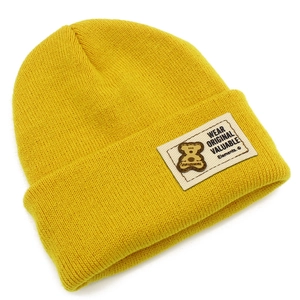 Détail d'un bonnet en tricot jaune vif avec un écusson blanc orné d'un petit ours brun