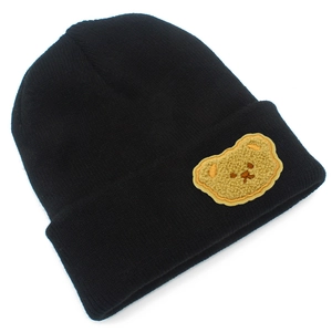 Dettaglio di un berretto in maglia nera con una toppa a forma di orsetto di peluche giallo