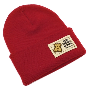 Détail du bonnet en maille rouge foncé montrant la texture côtelée et le patch ours