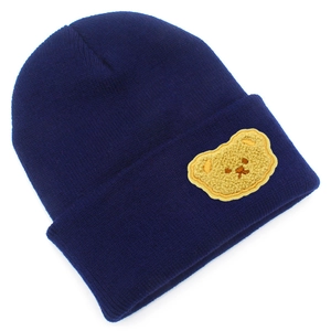 Dettaglio del berretto in maglia blu scuro con applicazione di orso giallo e risvolto