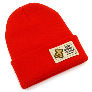 Détail du bonnet en tricot rouge vif à côtes avec écusson tissé arborant un logo d'ours