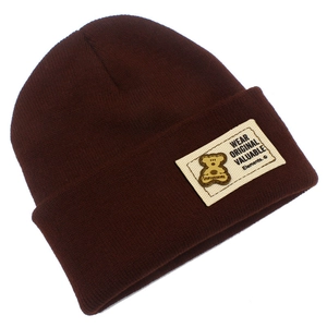 Détail du bonnet en maille marron foncé avec étiquette blanche et badge petit ours