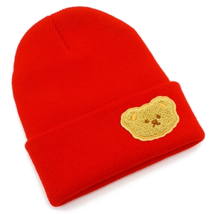 Dettaglio del berretto in maglia rossa con decorazione a toppa di orsetto giallo