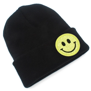 Détail du bonnet en maille noir avec un écusson smiley jaune scintillant sur le bord plié