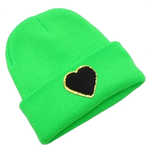 Close-up of bright green knitted beanie featuring a black heart patch with gold glitter edge