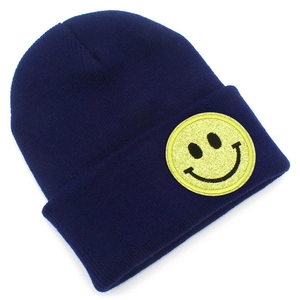 Détail du bonnet en maille bleu marine avec un écusson smiley à paillettes sur le bord plié