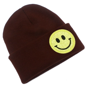 Gros plan d'un bonnet en tricot marron foncé avec un écusson smiley jaune à paillettes