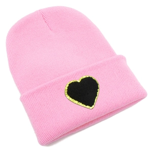 Detailed view of pink knitted beanie featuring a black heart patch with golden glitter edges