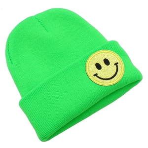 Détail d'un bonnet en tricot vert néon avec un écusson smiley jaune scintillant et brodé