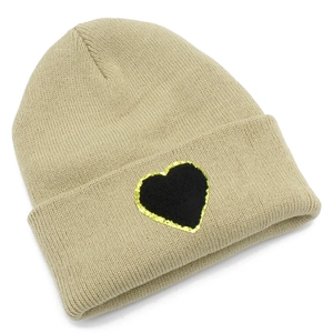 Detailed view of beige knit beanie featuring a black heart patch with gold glitter edges
