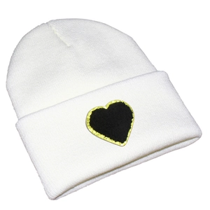Close-up of white knit beanie featuring a black heart patch with gold sequin border