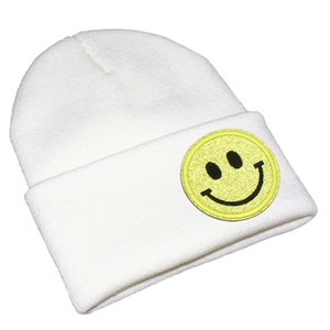 Détail d'un bonnet en maille blanche avec écusson smiley jaune brillant et revers