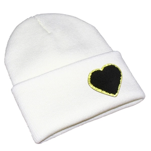 Detail view of a white knitted beanie featuring a black heart patch with gold sequin edges
