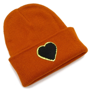 Detail of orange knit beanie featuring a black heart patch with gold sequin embroidery