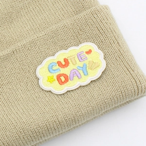 Gros plan détaillé d'un bonnet en maille beige avec un écusson brodé coloré Cute Day