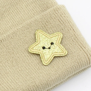 Close-up of khaki knitted star beanie with a golden sequin smiley face patch