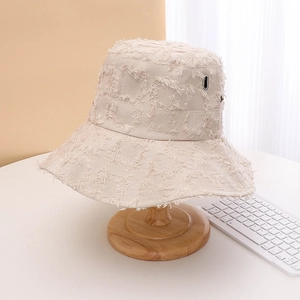 Close-up detail of the beige distressed bucket hat with wide brim on a wooden stand.