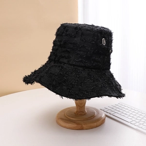 Close-up detail of black fringe bucket hat texture and metal ring accessory on wooden display.