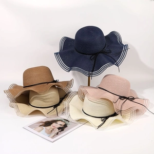 Detail view showing five colors of wide brim straw hats with wavy edges and bows