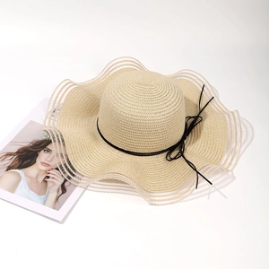 Detail of wide wavy brim straw sun hat with delicate black bow and airy striped weave