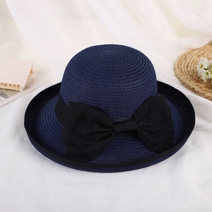 Detail of navy blue straw sun hat featuring a large black bow on a minimalist fabric background