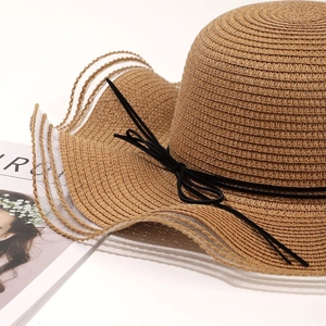 Detail of wavy brim straw sun hat featuring white mesh edge and delicate black bow tie