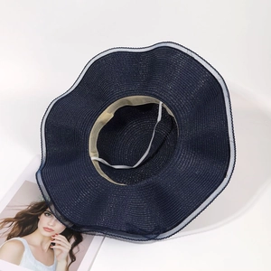 Détail d'un chapeau de soleil en paille bleu marine avec bord ondulé et mentonnière