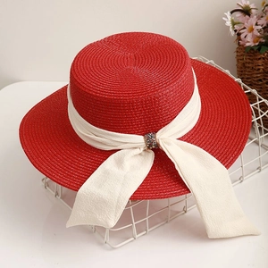 Elegant red boater straw hat with cream ribbon and jeweled buckle on a mesh basket