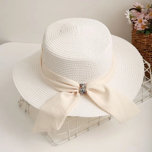 Detail of cream woven straw hat featuring a chic beige ribbon and colorful jewel buckle