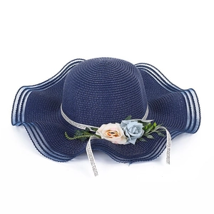 Detail of navy blue straw sun hat featuring elegant faux flowers and wavy brim design