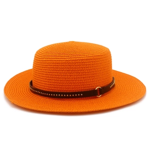 Detail of orange straw hat featuring dark brown leather band with gold studs and buckle