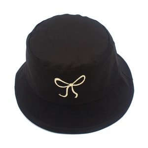 Close-up of golden bow embroidery on the crown of a black cotton fisherman hat