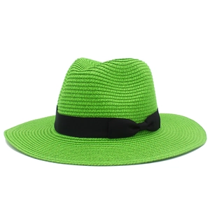 Detail of bright green woven straw hat featuring a black ribbon bow and natural texture