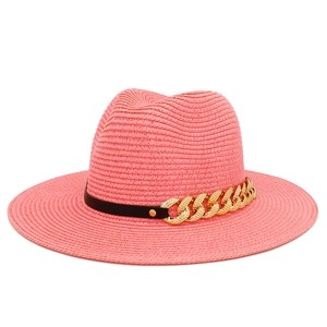 Détail d'un chapeau fedora en paille tressée rose corail avec ruban noir et chaîne dorée