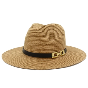 Dettaglio cappello di paglia a tesa larga con fascia nera e fibbia dorata su sfondo bianco