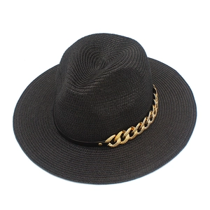 Détail d'un chapeau fedora en paille noire orné d'une chaîne dorée sur ruban de cuir chic