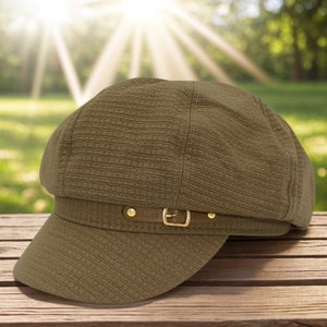 Detail of brown newsboy cap with leather strap and golden buckle on wooden surface