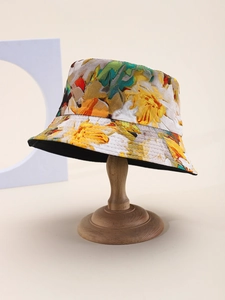 Detail of vibrant floral bucket hat with yellow and green patterns on a wooden stand