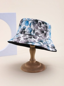 Detailed close-up of white sun hat with blue leaf print on a wooden display stand