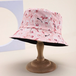 Pink floral bucket hat with cherry blossom pattern and black inner lining on wooden stand