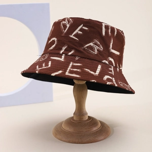 Minimalist brown canvas bucket hat with white graffiti text on a wooden display stand