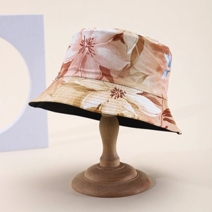 Floral print cotton bucket hat in warm orange and beige on a wooden display stand