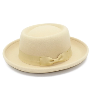 Detail view of beige wool pork pie hat featuring grosgrain ribbon and bow on plain background